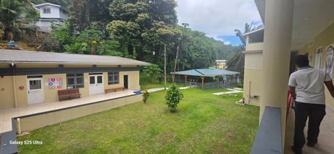 School or institutional buildings with green lawn and forested mountains in background, person walking on right side